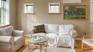 A living room with a white sofa, a round table with a tray, and two windows. - 3 bedroom cozy home in Havndal (Havndal)