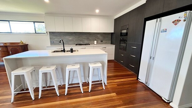 A modern kitchen with a central island, bar stools, a refrigerator, and a window. - Jaspa - River Views. (South West Rocks)
