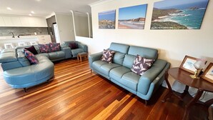 A modern living room with a blue sofa set, wooden flooring, and coastal artwork on the wall. - Jaspa - River Views. (South West Rocks)