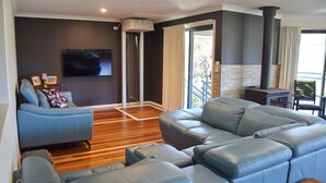 A modern living room with a blue sofa, a flat-screen TV, and a fireplace. - Jaspa - River Views. (South West Rocks)