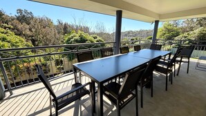 A covered outdoor area with a table and chairs, surrounded by a metal railing, overlooking a forested landscape. - Jaspa - River Views. (South West Rocks)