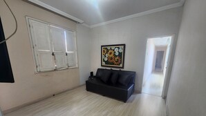 A spacious living room with a black sofa, a painting on the wall, and a door leading to another room. - 3 bedrooms with garage - Read the description  (Centro Juiz de Fora)