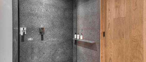 Un área de ducha moderna con cabina de vidrio, puerta de madera y repisa con artículos de aseo.