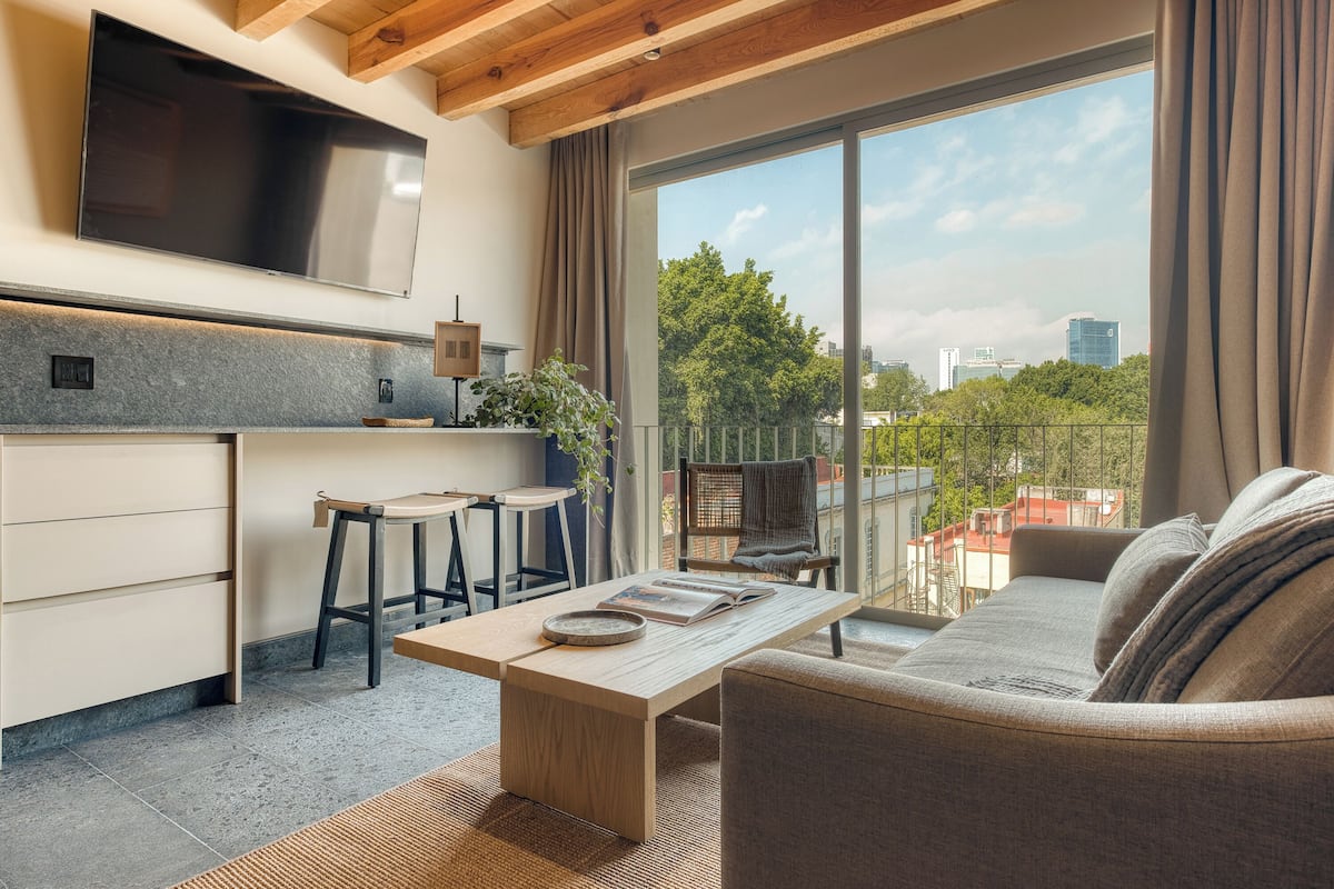 Una cocina moderna con un televisor grande, un comedor con mesa y sillas, y un sofá con vistas a la ciudad.
