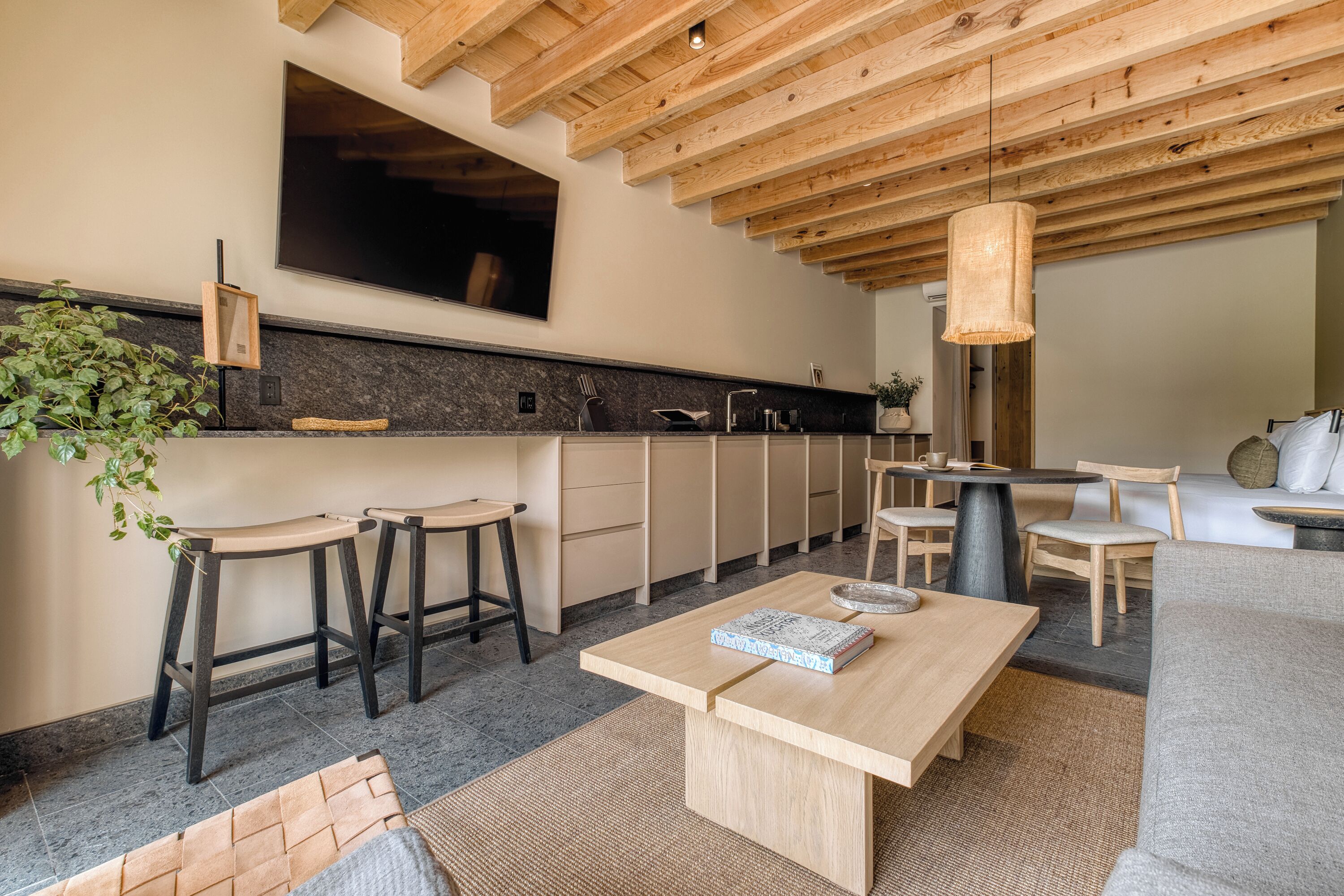 A modern kitchen with wooden beams, a large TV, bar stools, and a dining area with a table and chairs.