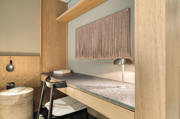A modern workspace with a wooden desk, a chair, a round stool, a lamp, and a textured wall hanging. - ONTO Alvaro Obregon Mexico City (Mexico City)