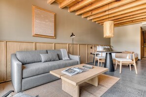 A modern living room with a grey sofa, a wooden coffee table, and a dining area with a table and chairs.