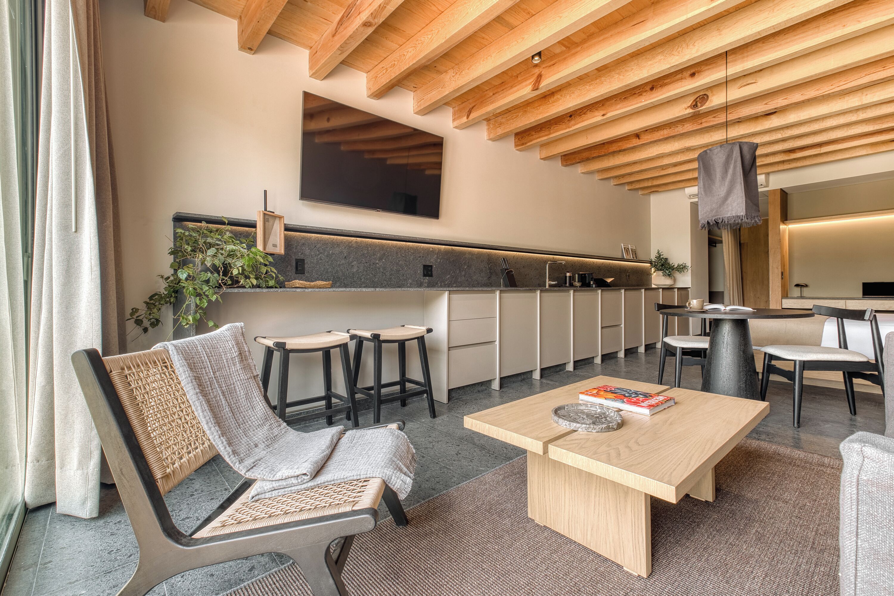 A modern kitchen with wooden beams, a large TV, and a bar area with stools.
