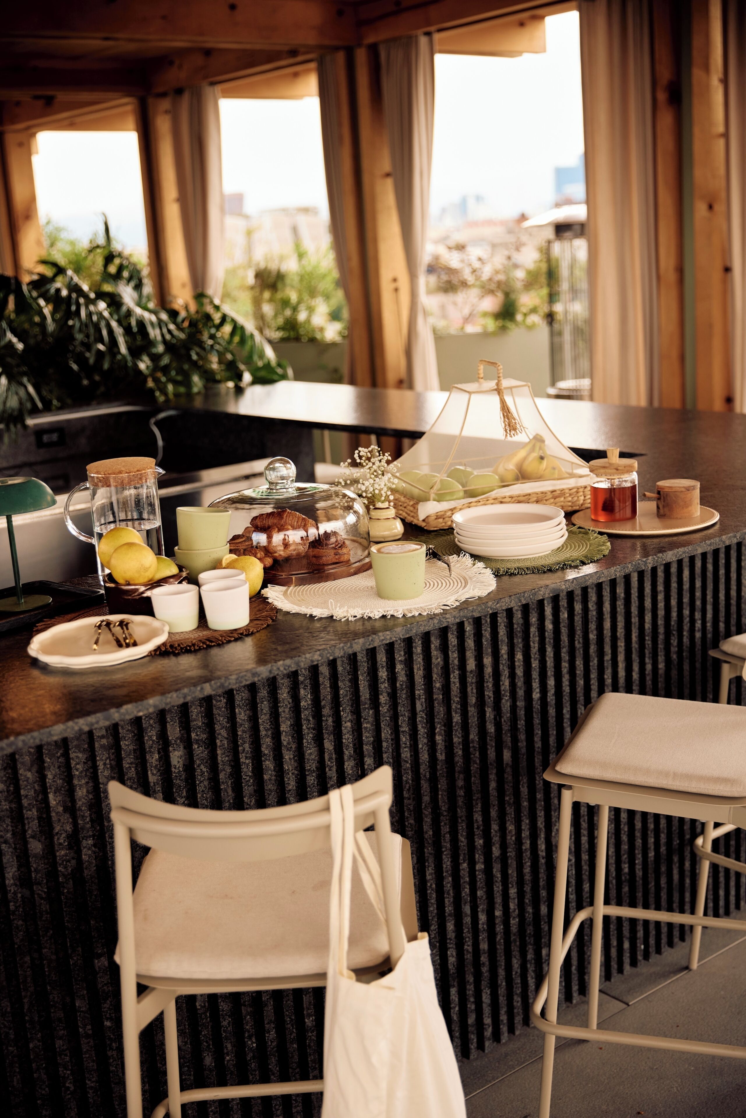 A bar area with a wooden counter, bar stools, and a view of the outdoors through large windows.
