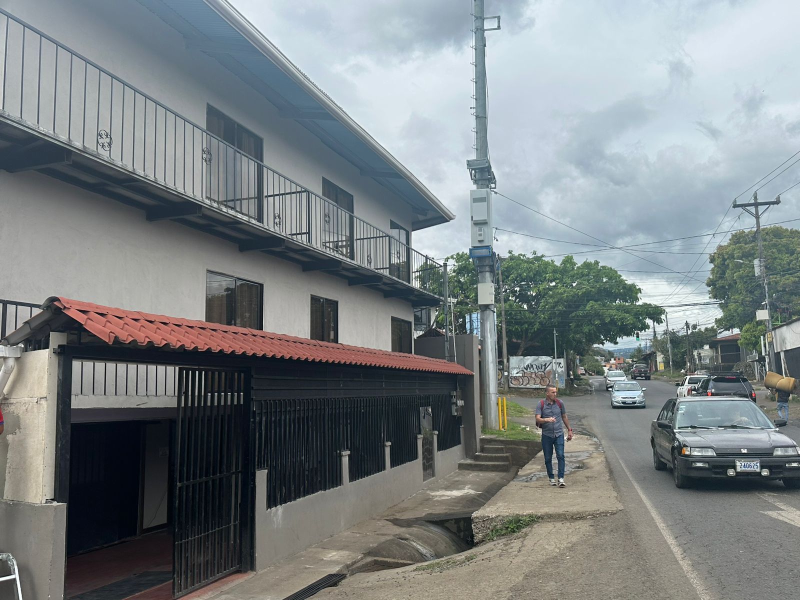 A street with a building featuring a red-tiled roof, a gated entrance, and a balcony.