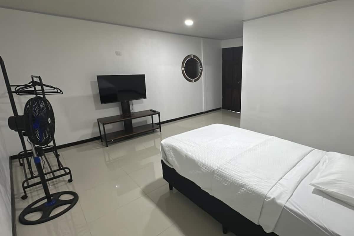 Un dormitorio con cama, televisor, ventilador y un adorno circular en la pared.