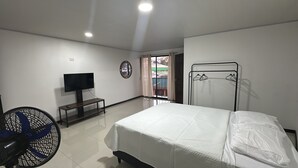 Ein Schlafzimmer mit einem Bett, einem Fernseher auf einem Schrank, einem Ventilator und einem Fenster mit Vorhängen.