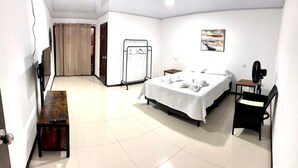 Ein Hotelzimmer mit Bett, Schreibtisch, Stuhl, Fernseher, Kleiderhaken und einer Tür.