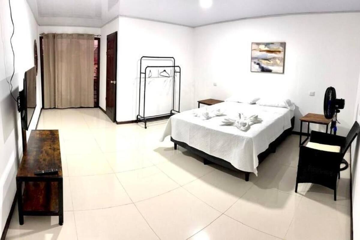 Una habitación de hotel con cama, escritorio, silla, televisión, perchero y puerta.