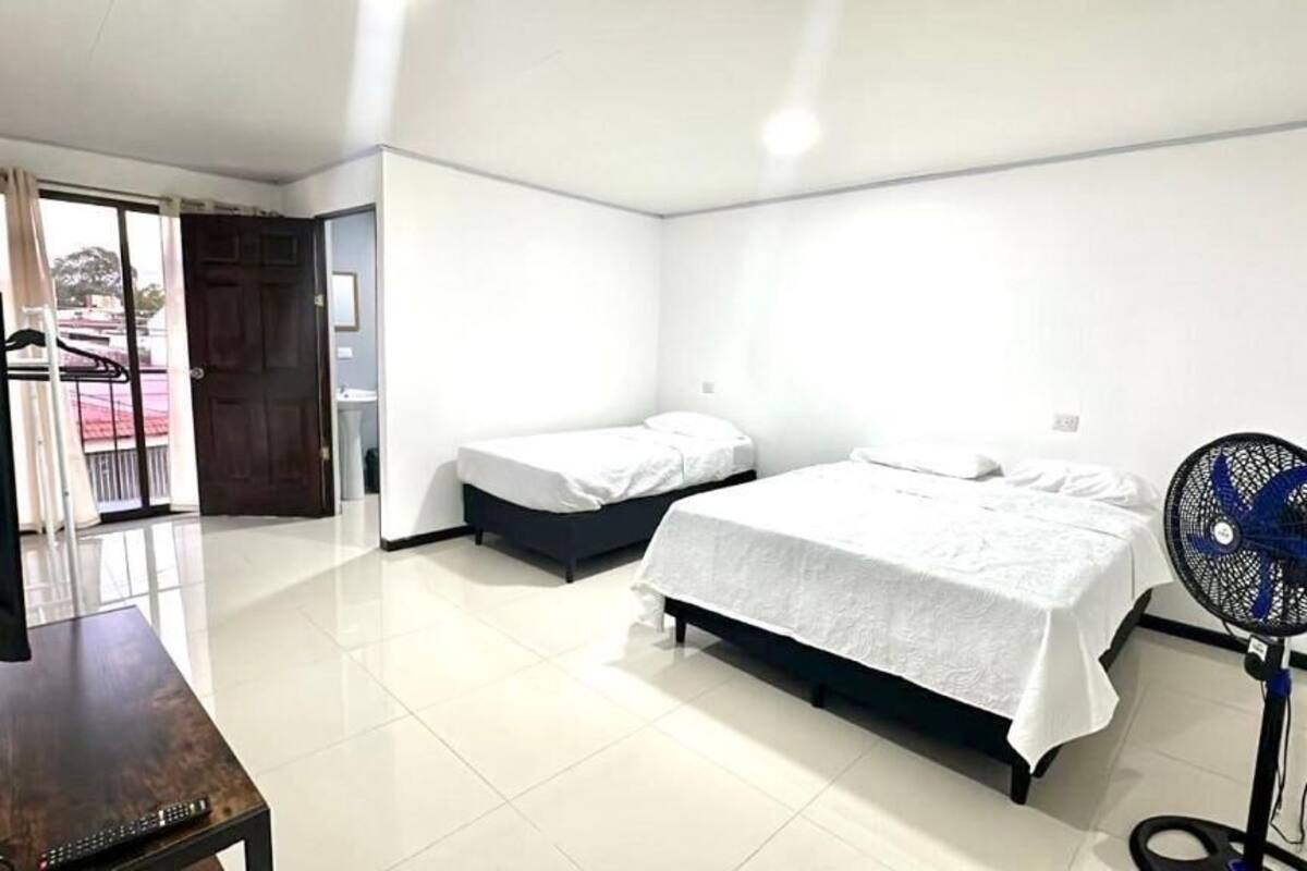 Habitación de hotel con dos camas, televisión, ventilador y balcón con vistas.