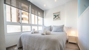 A bedroom with a large bed, a nightstand, a wall-mounted artwork, and a window with blinds. - MalagaSuite Dreams of Torremolinos (Torremolinos)