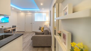 A modern living room with a sofa, a dining area with a table and chairs, a kitchen area with a sink, and a TV mounted on the wall. - MalagaSuite Dreams of Torremolinos (Torremolinos)