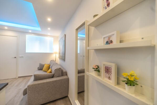 A modern living room with a sofa, a coffee table, and a bookshelf with framed pictures and a vase of flowers.