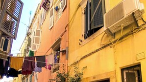 A narrow cobblestone street lined with colorful buildings, featuring balconies with drying laundry and potted plants.