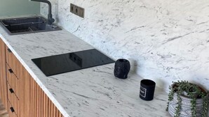 A modern kitchen with a marble countertop, wooden cabinets, and a built-in sink. - Anamar Apt (Alepou)