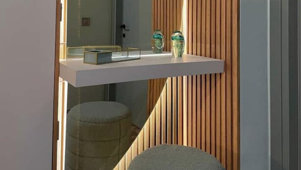 A modern bathroom with a wooden slat wall, a floating shelf with decorative items, and a round stool. - Anamar Apt (Alepou)