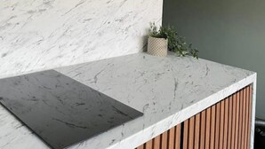 A kitchen with a marble countertop, wooden cabinets, and a small potted plant. - Anamar Apt (Alepou)