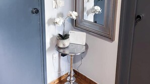 A corner of a room with a grey door, a small round table with a potted orchid, a mirror, and a wall-mounted telephone. - Downtown Oasis (Kerkira)