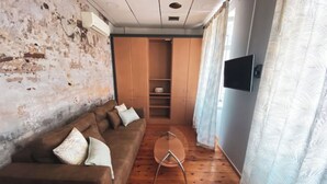 A room with a brown sofa, a small round table, wooden flooring, a TV on the wall, and a wardrobe. - Downtown Oasis (Kerkira)