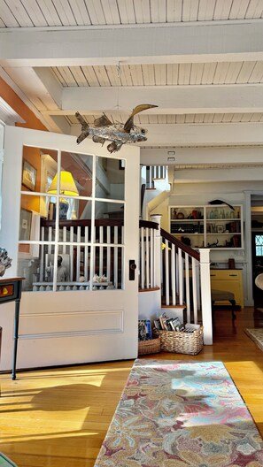 A spacious living room with a wooden floor, a colorful rug, a staircase with a white railing, and a fish sculpture hanging from the ceiling.