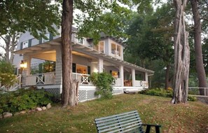 A two-story house with a porch, surrounded by trees and a grassy yard.