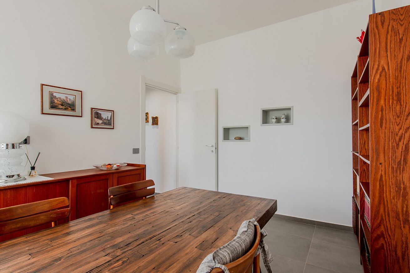 Una cocina moderna con una mesa de madera, paredes blancas y un mueble de estanterías de madera empotrado.