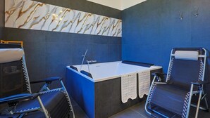 A modern bathroom with a marble wall, a bathtub, and two chairs. - Villa Scini by Rentbeat (Roma)