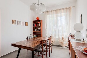 A dining area with a wooden table, chairs, a bookshelf, and a window with sheer curtains. - Villa Scini by Rentbeat (Roma)
