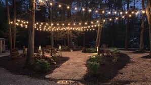 A stone pathway leading to a wooden deck surrounded by trees, with string lights overhead. - Creekside Tiny house in fantastic Monteagle! Quick hike to waterfall!  (Monteagle)