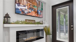A modern living room with a fireplace, a mounted TV, and a door with a view of the outdoors. - Creekside Tiny house in fantastic Monteagle! Quick hike to waterfall!  (Monteagle)