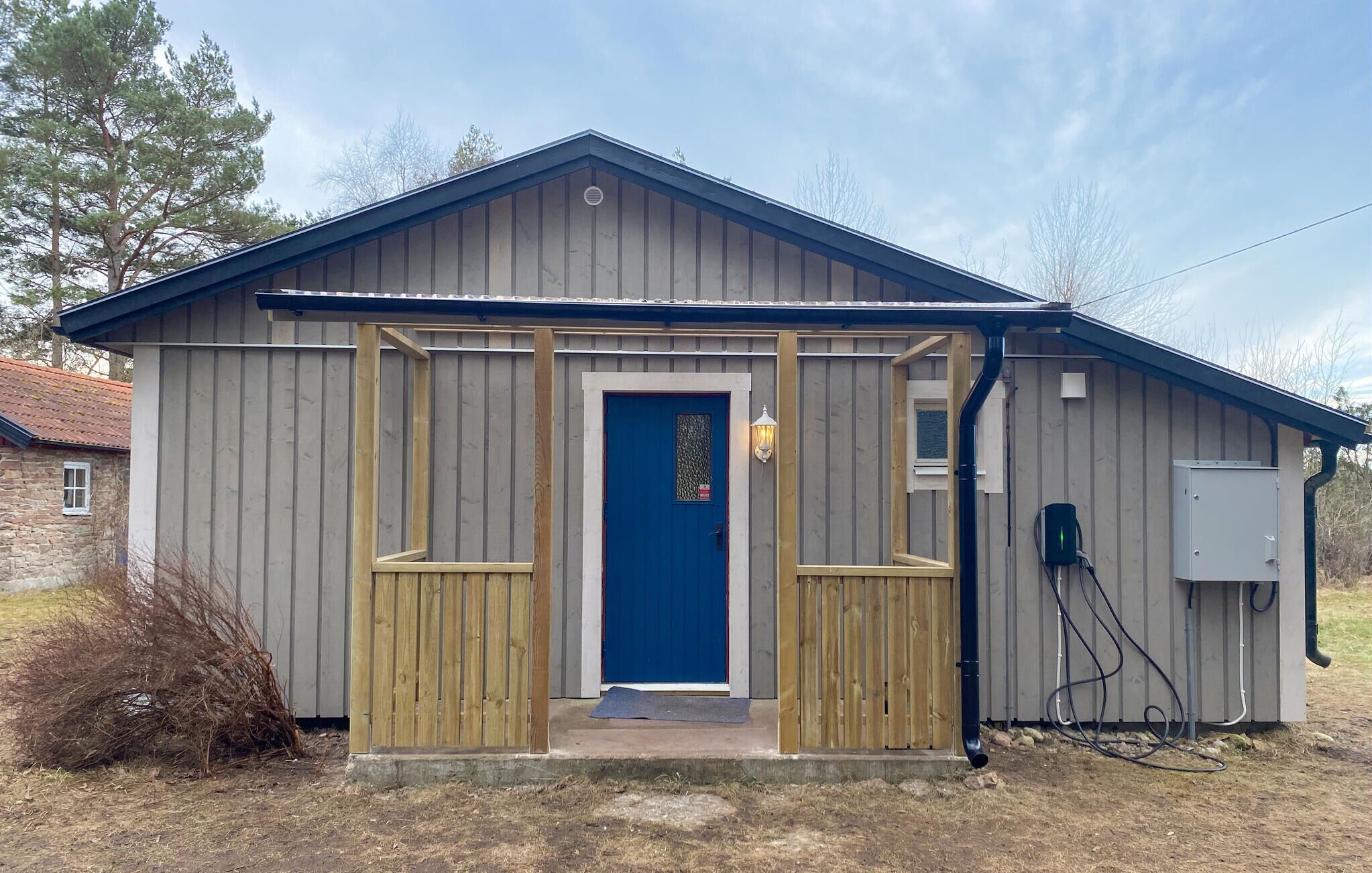 Ein kleines, eingeschossiges Gartenhaus mit einer blauen Tür, Holzrahmen und einem Metalldach.
