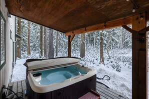 A hot tub under a wooden pergola with a snowy forest view.