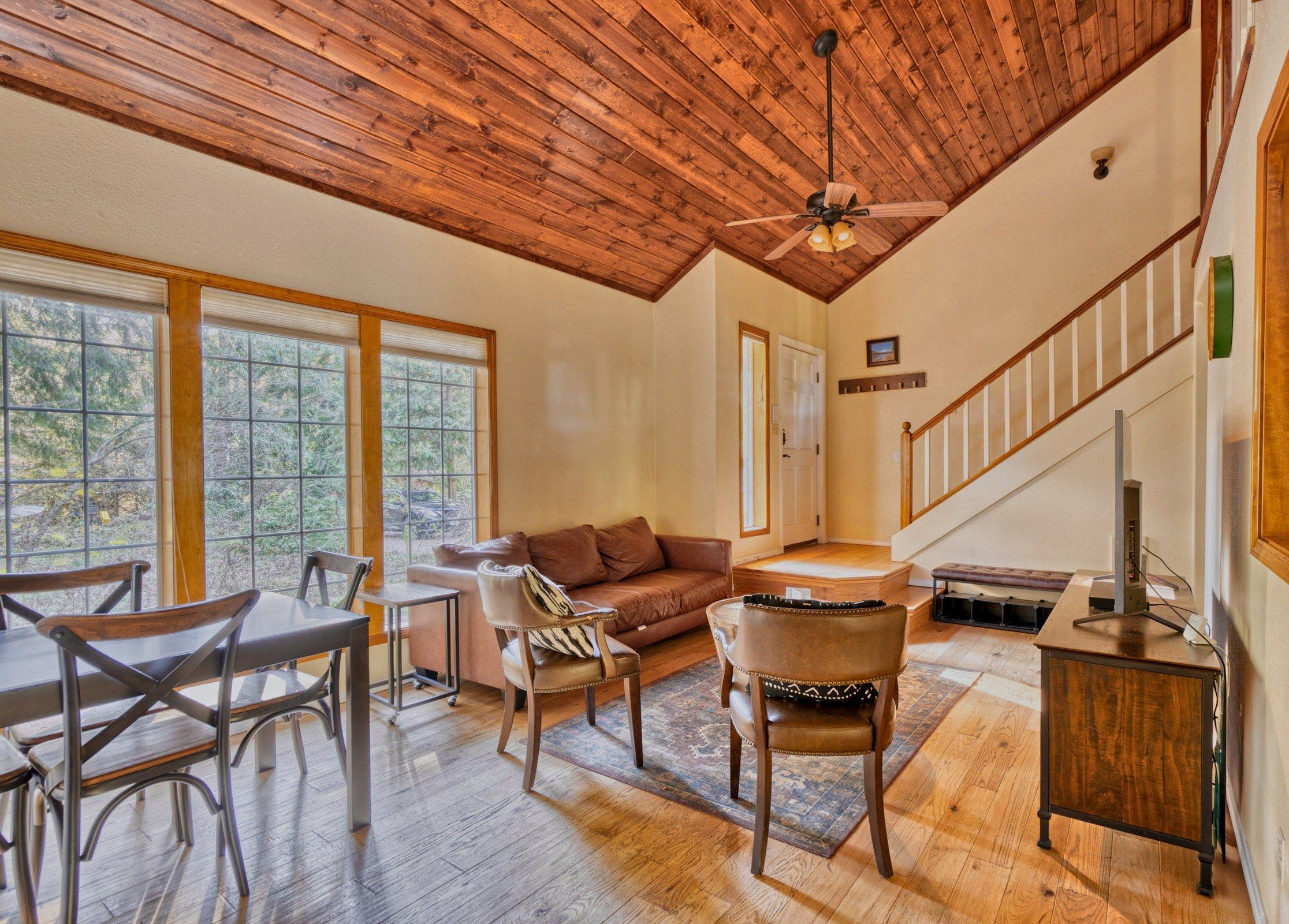 A spacious living room with a wooden ceiling, a sofa, a dining table with chairs, and a staircase.