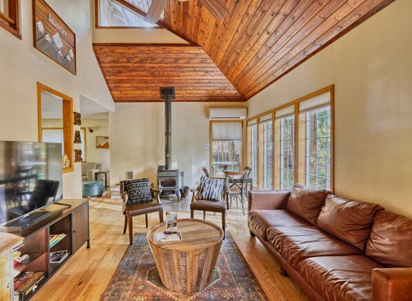 A spacious living room with a high ceiling, wooden beams, a leather sofa, a television, and a fireplace.