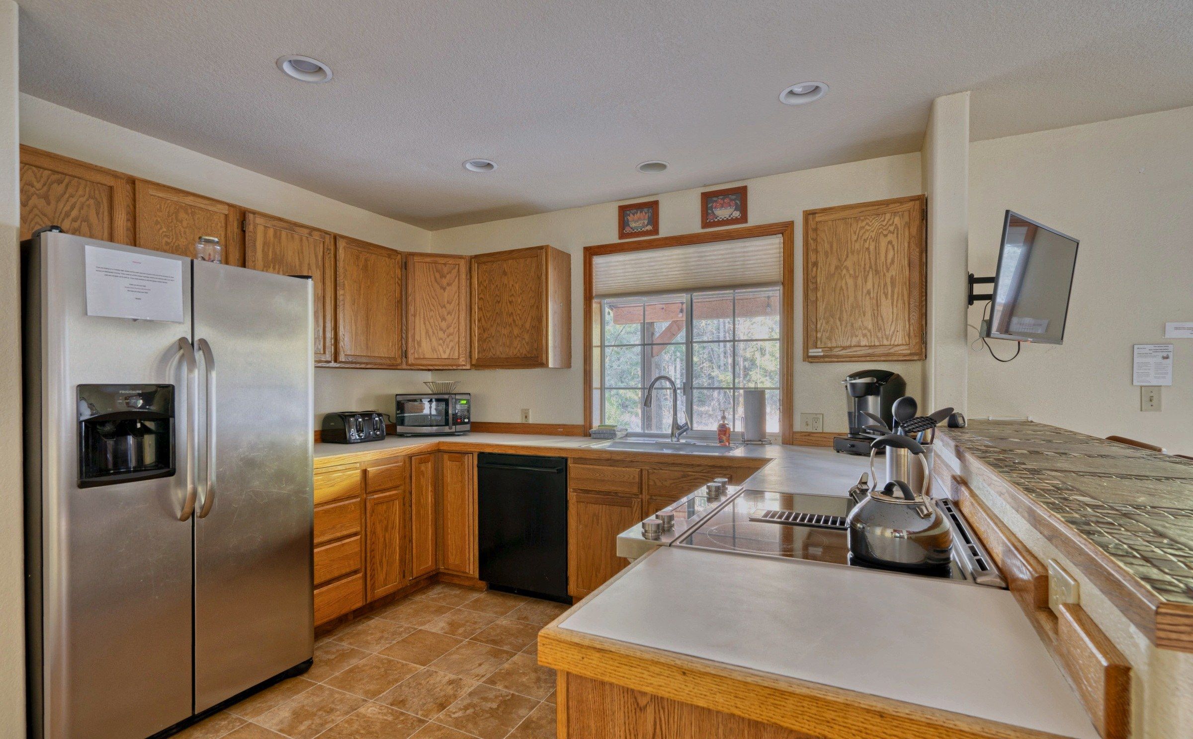 A kitchen with wooden cabinets, a stainless steel refrigerator, a dishwasher, a sink, and a kettle.