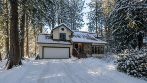 Una casa de dos pisos con garaje, rodeada de árboles cubiertos de nieve.