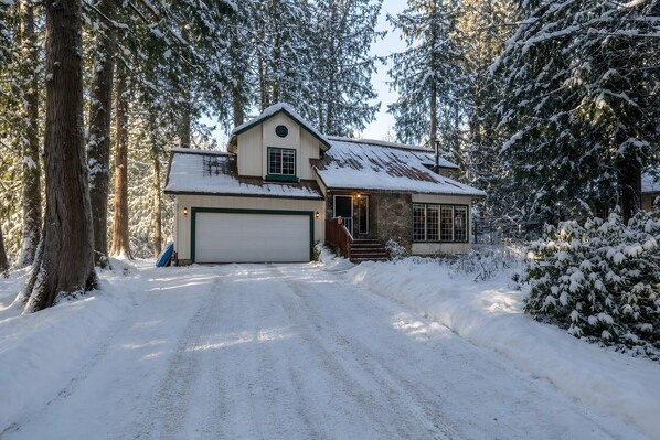 A two-story house with a garage, surrounded by snow-covered trees.
