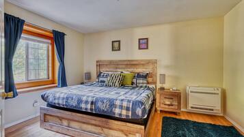 A bedroom with a wooden bed, a window with curtains, a wall-mounted air conditioner, and two framed pictures.
