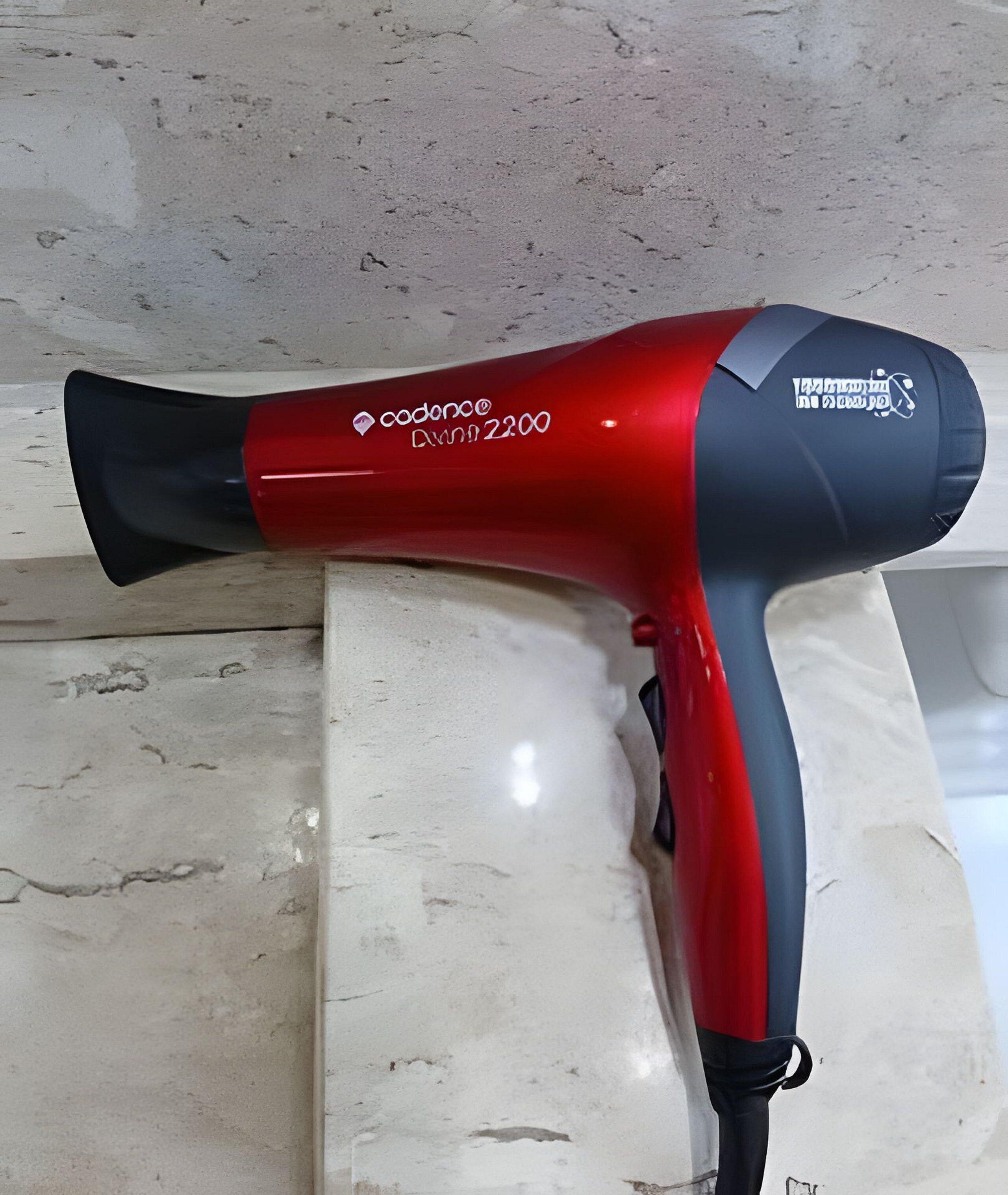 A red and black hair dryer with a cord, placed on a marble surface.