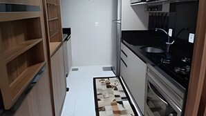 A compact kitchen with wooden cabinets, a microwave, a sink, and a tiled backsplash. - Siga Gramado -Ap Lindíssimo 5 min Centro (Gramado)