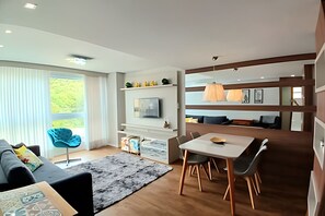 Un salon moderne avec un canapé, une table à manger et un téléviseur. Il y a une grande fenêtre avec des rideaux, un tapis et un plancher en bois.