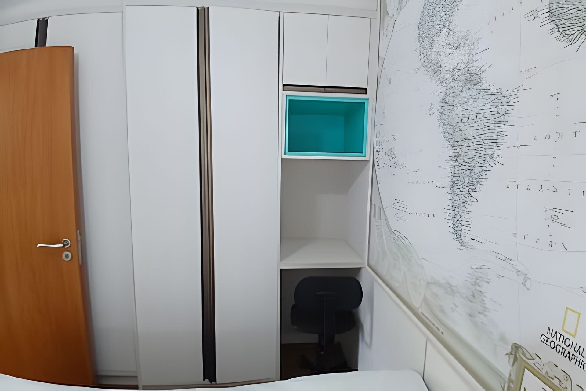 A room with a wooden door, a white wardrobe with a teal storage box, and a black office chair.