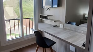 A modern hotel room with a large window, a flat-screen TV mounted on the wall, a wooden desk, and a black chair. - Siga Gramado -Ap Lindíssimo 5 min Centro (Gramado)