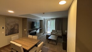 Un salon moderne avec une table à manger en bois, des chaises blanches, un canapé et un téléviseur fixé au mur.
