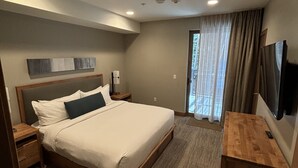 Une chambre d’hôtel avec un grand lit, une table de chevet en bois, un téléviseur à écran plat et une vue sur l’extérieur par une fenêtre munie de rideaux.